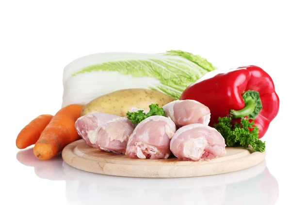 Свежие овощи с сырыми куриными барабанными палочками и свиным стейком на разделочной доске изолированы на белом — стоковое фото