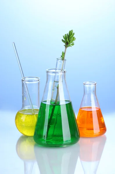 Különböző laboratóriumi üvegeszközök, kék alapon, színes folyadékkal — Stock Fotó