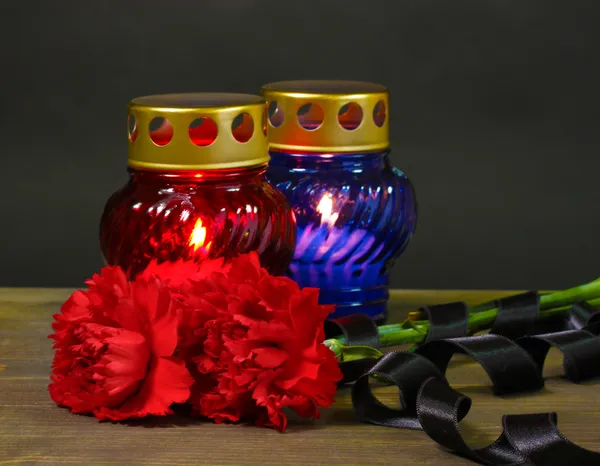 Linterna de memoria con velas, claveles rojos y cinta sobre mesa de madera sobre fondo gris — Foto de Stock