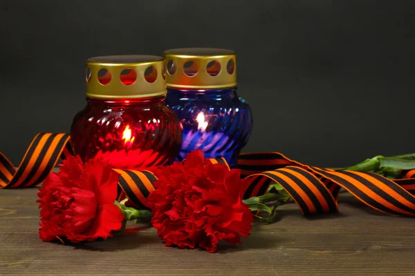Фонарь памяти со свечами, красными гвоздиками и Георгиевской лентой на деревянном столе на сером фоне — стоковое фото