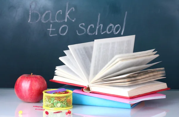 Könyvek, papíráruk és az alma, a háttérben a táblára a tanári asztalon összetétele. vissza az iskolába. — Stock Fotó