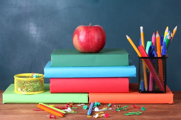 Composition of books, stationery and an apple on the teacher's desk in the background of the blackboard — Stock Photo, Image