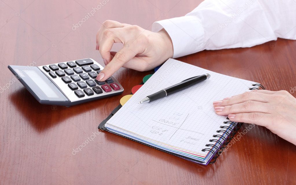 Women hands with pencil, notebook and Calculator on wooden table