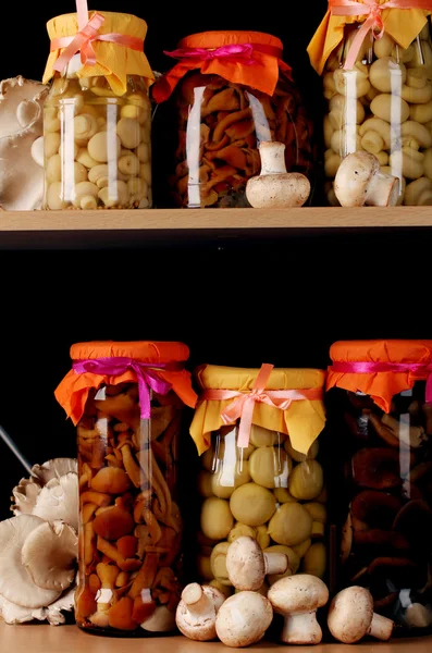 Deliciosos cogumelos marinados nos frascos de vidro, champinhons crus e cogumelos de ostra em prateleiras de madeira — Fotografia de Stock