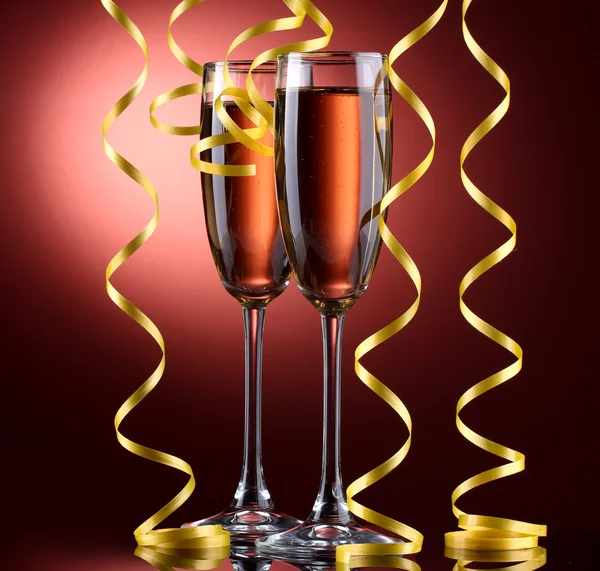 Copos de champanhe e streamer no fundo vermelho — Fotografia de Stock