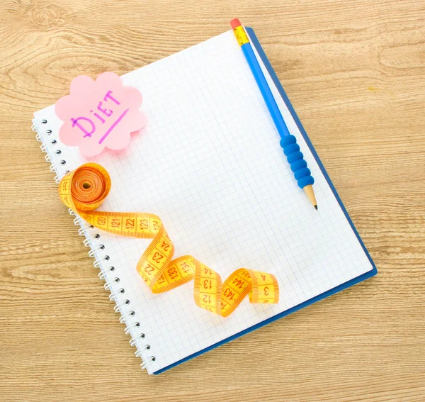 Pianificazione di dieta. Nastro di misurazione e penna per notebook su tavolo in legno — Foto Stock