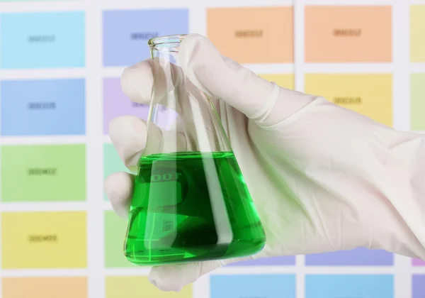 Flask con liquido verde in mano su sfondo campioni di colore — Foto Stock