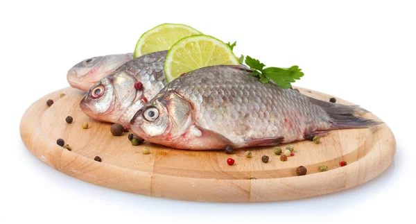 Peces frescos con lima, perejil y especias sobre tabla de cortar de madera aislada en blanco — Foto de Stock