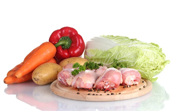 Fresh vegetables with raw chicken drumsticks and pork steak on cutting board isolated on white — Zdjęcie stockowe