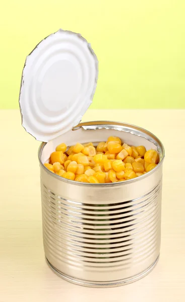 Open tin can of corn on wooden table on green background — Stock Photo, Image