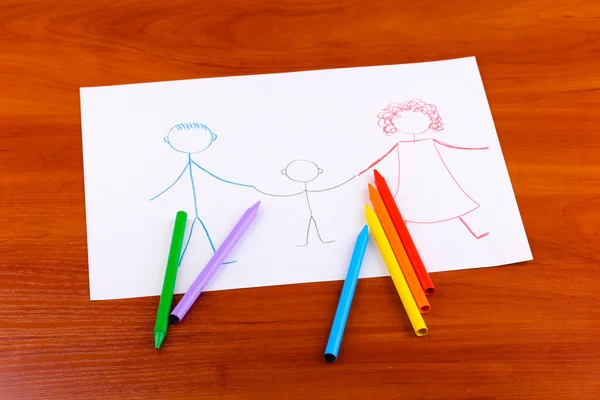 Children's drawing of family and pencils on wooden background — Stock Photo, Image