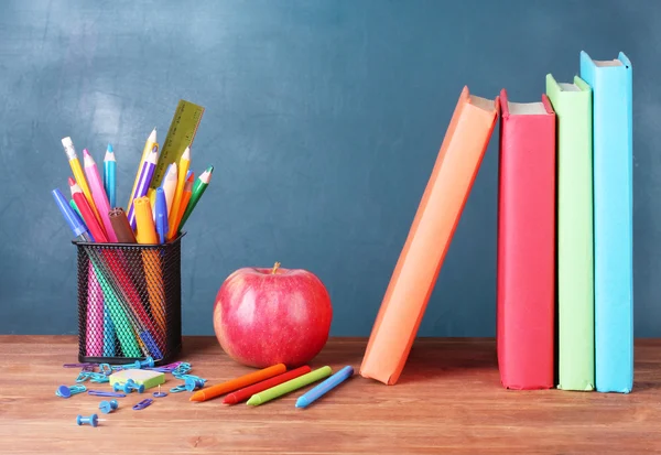 Sammansättningen av böcker, pappersvaror och ett äpple på lärarens skrivbord i bakgrunden i tavlan — Stockfoto