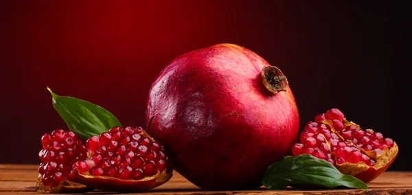 Modne granateplefrukter med blader på trebord på rød bakgrunn – stockfoto