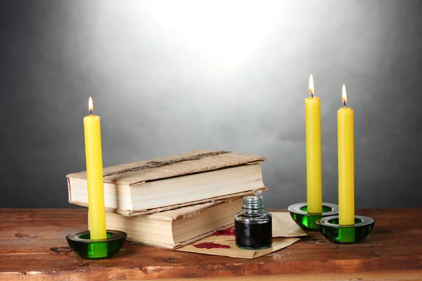 Stare książki, przewija, atrament długopis Kałamarz i świece na drewnianym stole na szarym tle — Zdjęcie stockowe