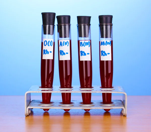 Tubos de ensayo con sangre sobre mesa de madera sobre fondo azul —  Fotos de Stock