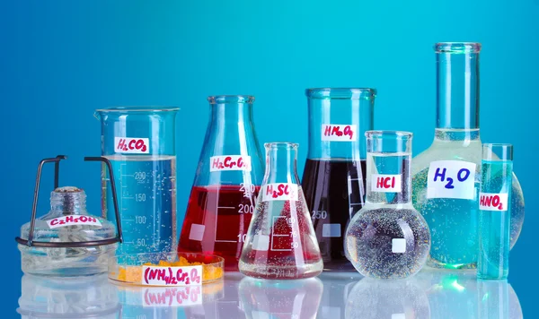 Tubos de ensayo con diversos ácidos y sustancias químicas sobre fondo azul — Foto de Stock