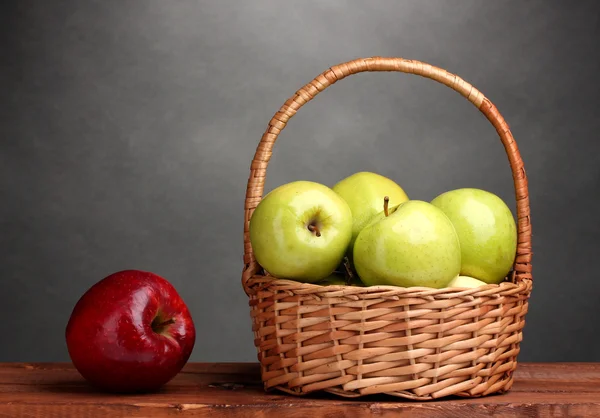 stock image Juicy green apples in basket and red apple on wooden table on gray background