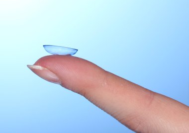 Contact lens on finger on blue background clipart