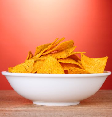 Tasty potato chips in white bowl on wooden table on red background clipart