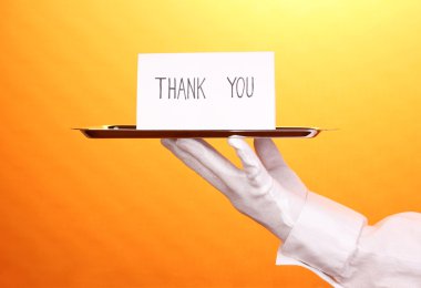 Hand in glove holding silver tray with card saying thank you on yellow background clipart