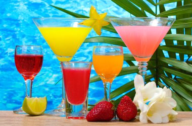 Exotic cocktails and flowers on table on blue sea background clipart