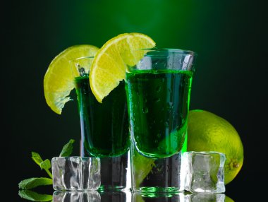 Two glasses of absinthe, lime and ice on green background clipart