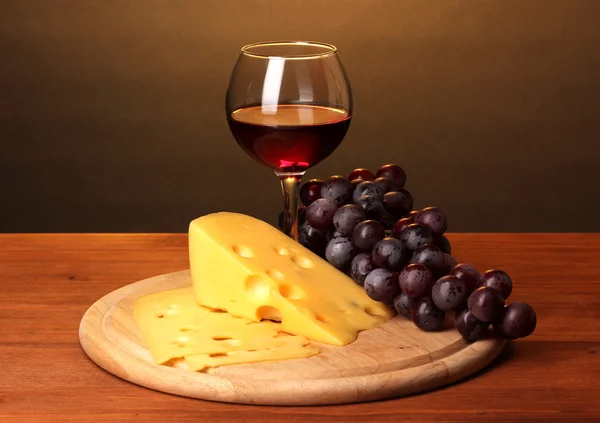 Wine in wineglass and cheese on wooden table on brown background — Stock Photo, Image
