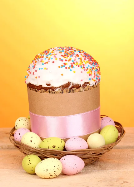 Hermoso pastel de Pascua en cesta con huevos en mesa de madera sobre fondo amarillo — Foto de Stock