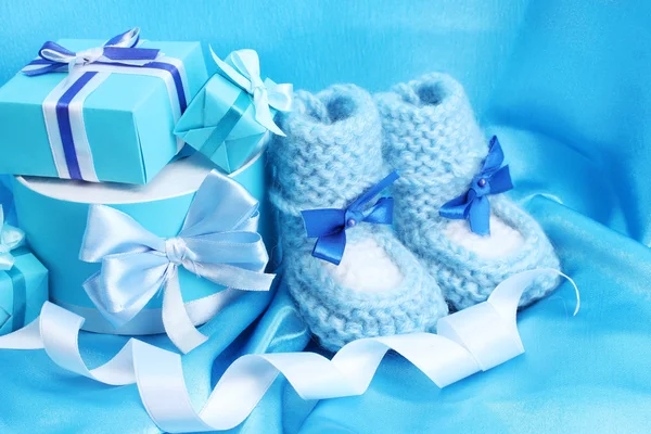 Schöne Geschenke und Babystiefel auf blauer Seide — Stockfoto