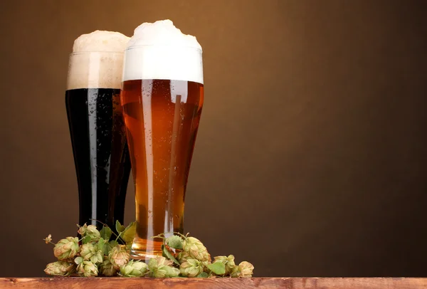 Zwarte en gouden bier in glazen en hop op houten tafel op bruine achtergrond — Stockfoto
