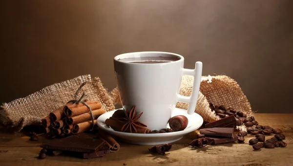 Tasse de chocolat chaud, bâtonnets de cannelle, noix et chocolat sur table en bois sur fond brun — Photo