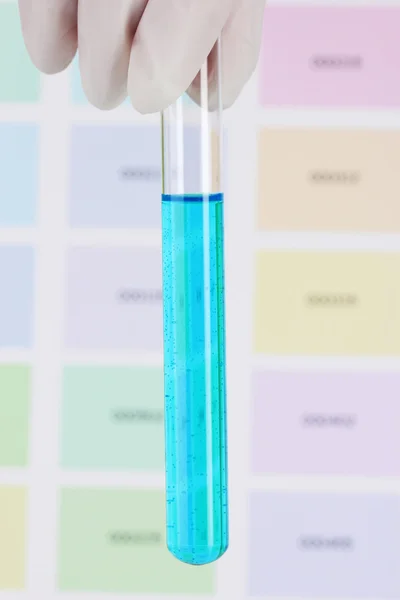 Tubo com líquido azul na mão em fundo de amostras de cor — Fotografia de Stock