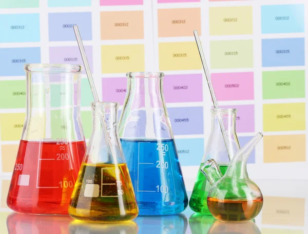 Лабораторные колбы с цветной жидкостью на фоне цветных образцов — стоковое фото