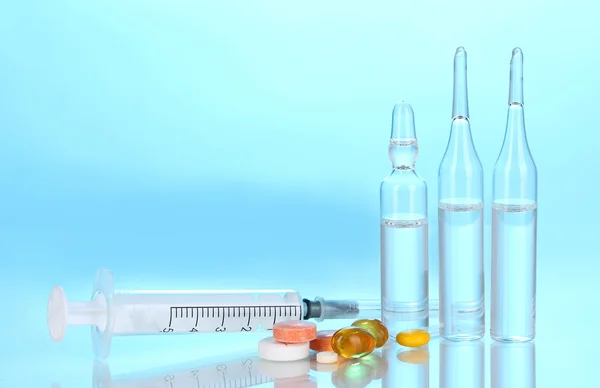 Spruta med medicinska ampuller och tabletter på blå bakgrund — Stockfoto