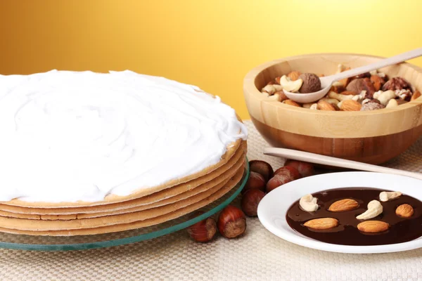 Cake on glass stand and nuts on table on yellow background — Stock Photo, Image