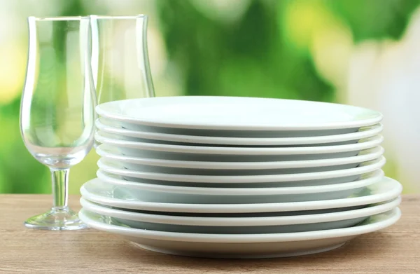 Czyste naczynia na drewnianym stole na zielonym tle — Zdjęcie stockowe