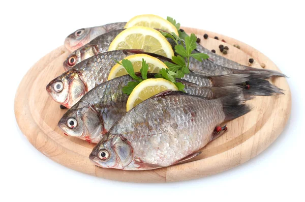 Peixes frescos com limão, salsa e especiarias em tábua de corte de madeira isolada em branco — Fotografia de Stock