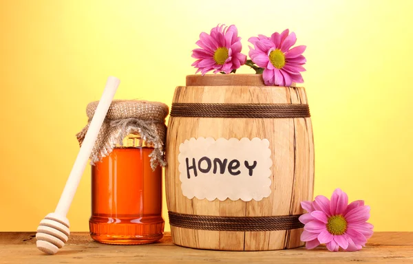 Солодкий мед в бочці і банку з мрякою на дерев'яному столі на жовтому фоні — стокове фото