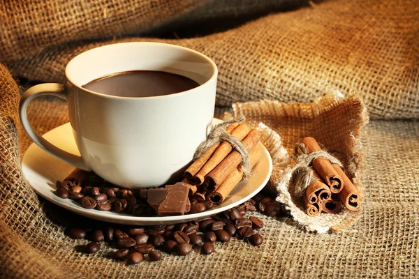 Taza de café y frijoles, palitos de canela y chocolate sobre fondo de saco — Foto de Stock