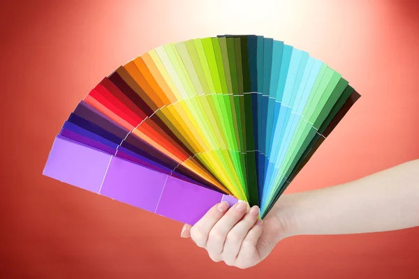 Ruka držící světlé palety barev na červeném pozadí — Stock fotografie