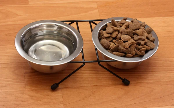 Dry dog food and water in metal bowls on the floor