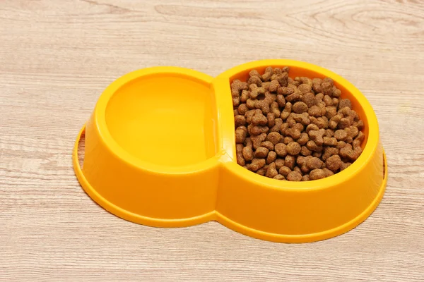 Suché krmivo pro kočky a voda v žluté misce na dřevěné pozadí — Stock fotografie