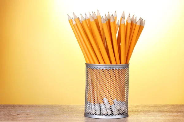 Lead pencils in metal cup on wooden table on yellow background — Stock Photo, Image