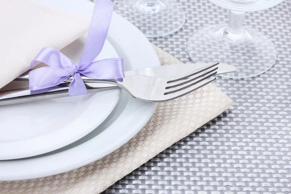 Weiße leere Teller, Gabel und Messer mit Band und Gläsern auf einer grauen Tischdecke gebunden — Stockfoto