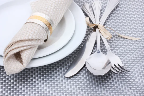 Beyaz boş tabak çatal, kaşık ve bıçak ile bir şerit üzerinde gri bir masa örtüsü ile bağlıdır. — Stok fotoğraf