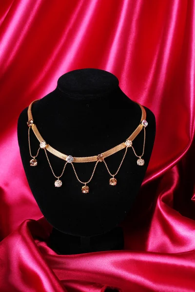 Beautiful golden necklace on mannequin on red silk fabric — Stock Photo, Image