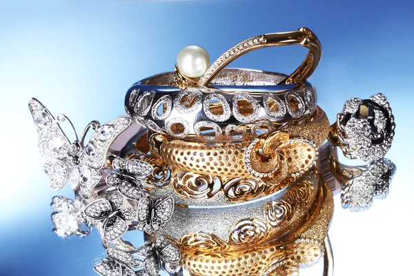 Pulseiras de prata e ouro bonitas e anéis no fundo azul — Fotografia de Stock