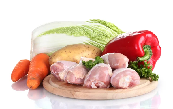 Fresh vegetables with raw chicken drumsticks and pork steak on cutting board isolated on white — Stock Photo, Image