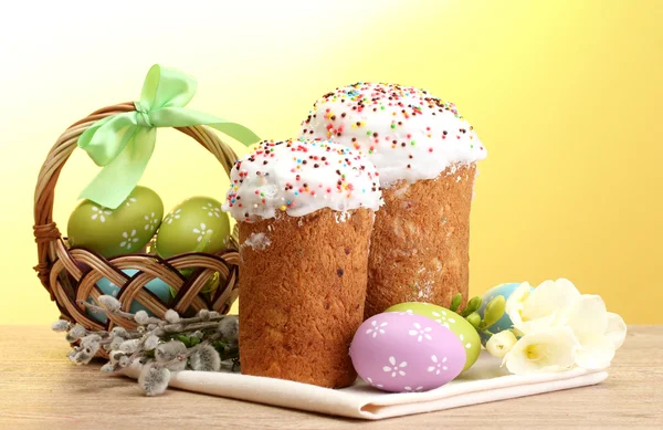 漂亮的复活节蛋糕、 篮子和阴部柳树枝在黄色背景上的木桌上丰富多彩的蛋 — 图库照片