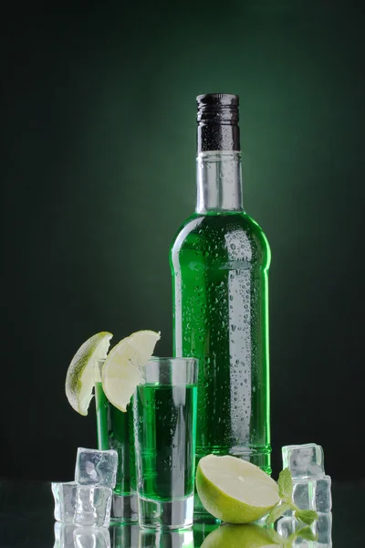 Pullo ja lasit absinttia kalkilla ja jäällä vihreällä pohjalla — kuvapankkivalokuva